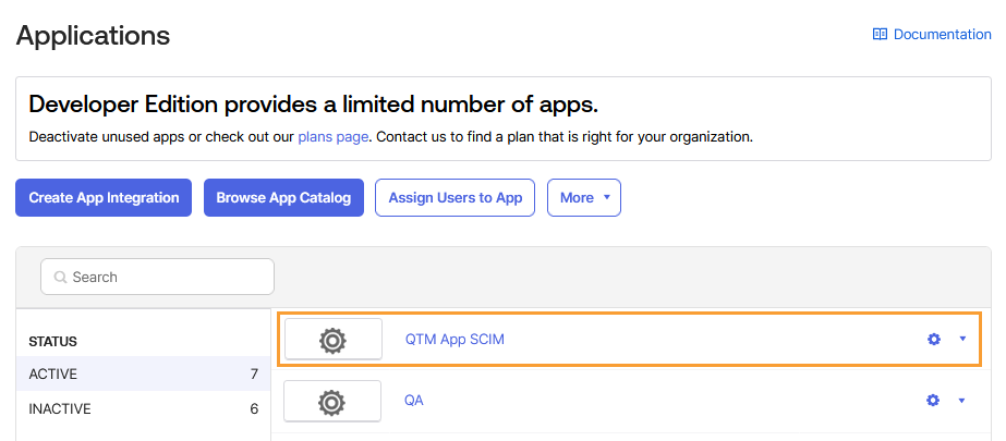Select QTM App SCIM from Okta Applications Okta Applications page displaying a list of available apps. The QTM App SCIM entry is highlighted under the “ACTIVE” section, showing the app’s gear icon and settings menu. Buttons for Create App Integration, Browse App Catalog, Assign Users to App, and More appear at the top of the screen.